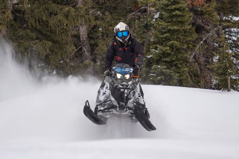Rider throwing powder on a mountain performance Polaris snowmobile