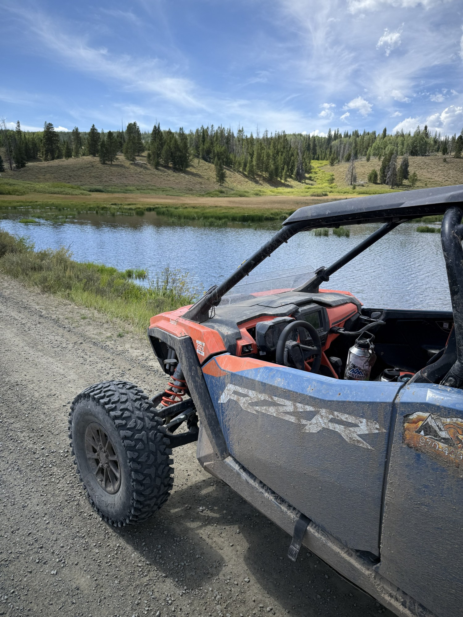 Off-road vehicle parked by a lake with hills and trees in the background.