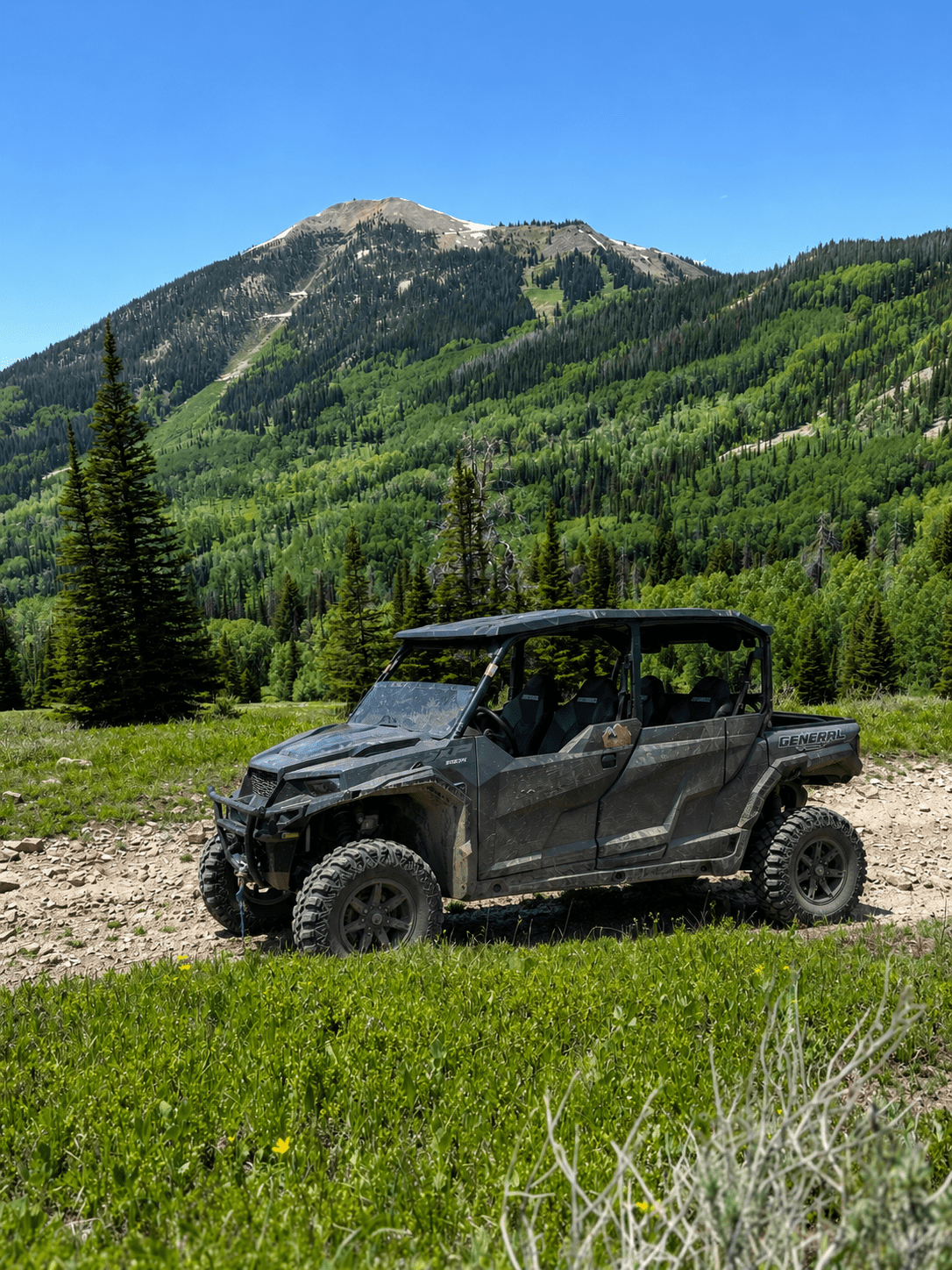 Off-road vehicle on rocky path with forested mountain background.