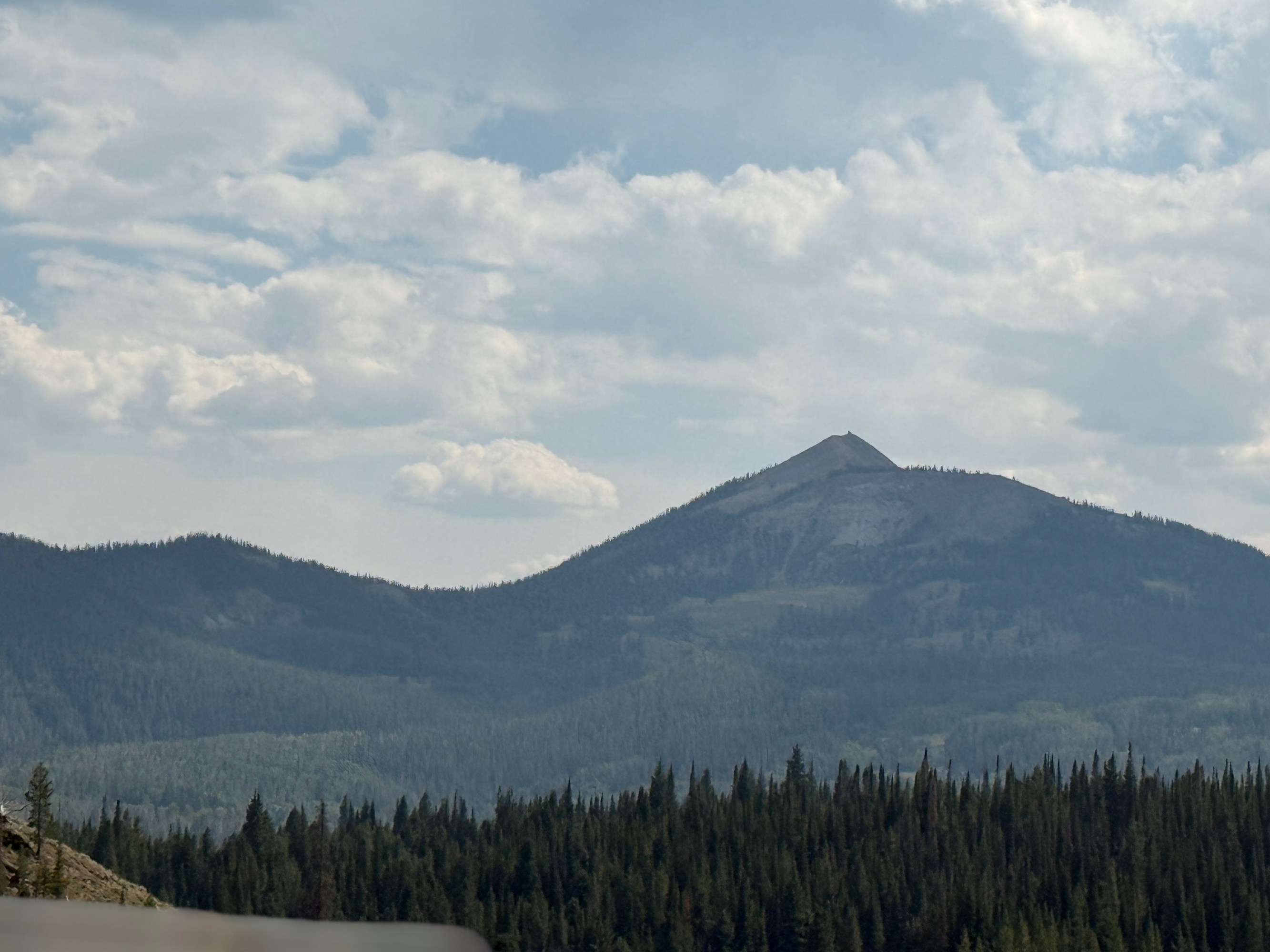 Mountain landscape with cloudy sky and forested foreground.