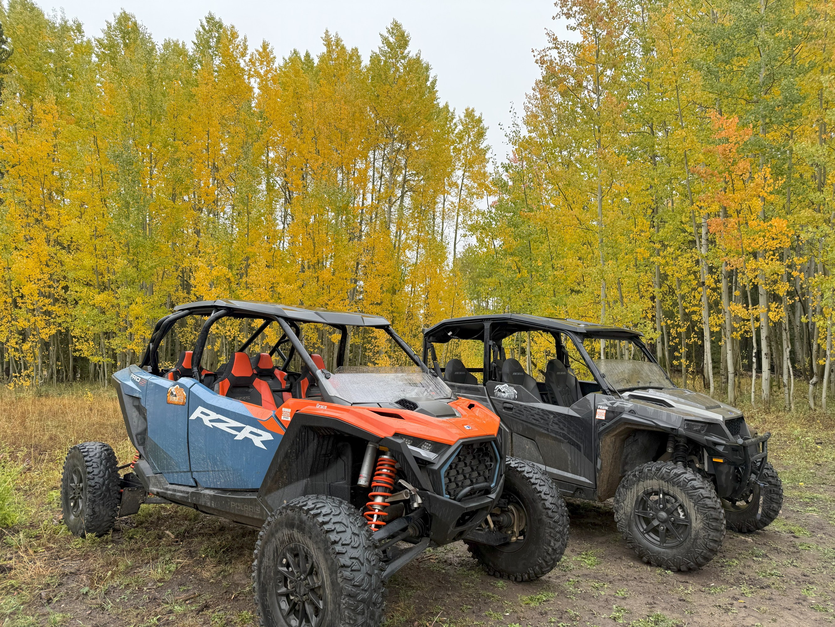 Two off-road vehicles parked in front of vibrant autumn trees.