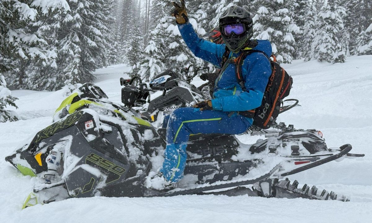 Smiling rider waving from a rented Polaris snowmobile in deep snow