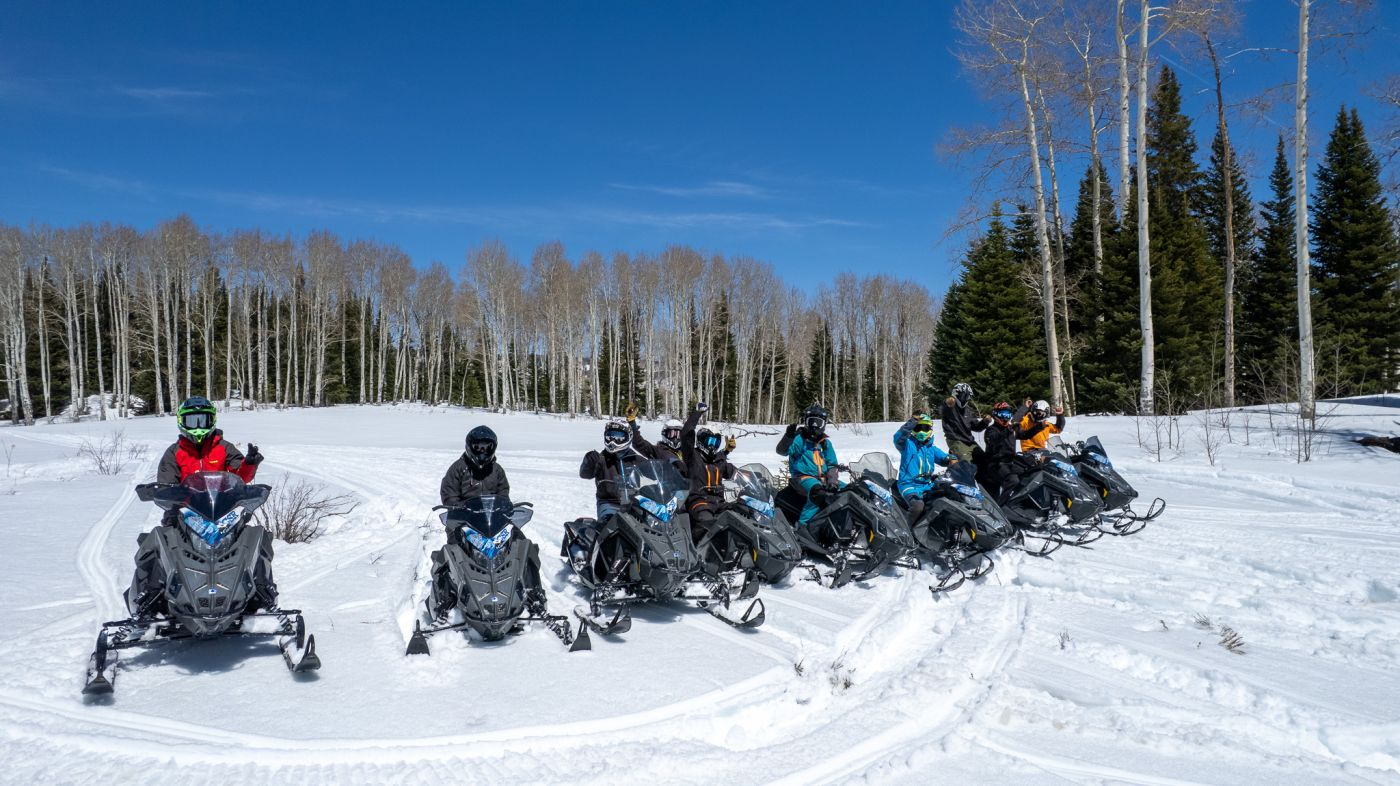 A group of Colorado Sled Rentals riders lined up on Polaris snowmobiles in a sunny aspen meadow